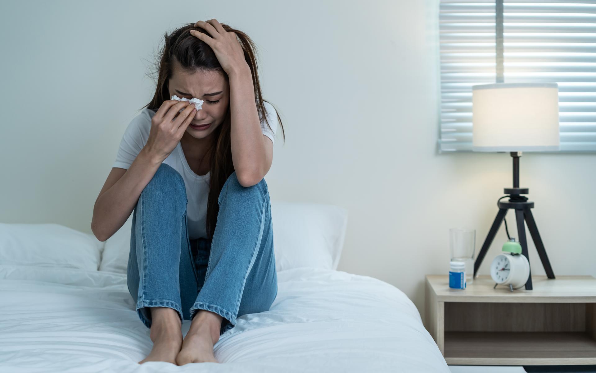 Junge Frau sitzt weinend im Bett