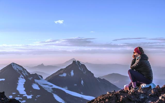eine-frau-sitzt-auf-einem-berg-neben-schneebedeckten-bergen