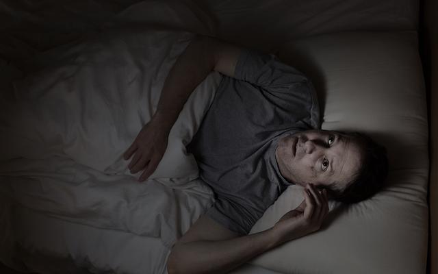 Mann liegt schlaflos im Bett