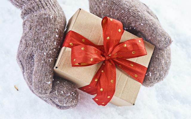 Hände in Handschuhen halten ein Geschenk