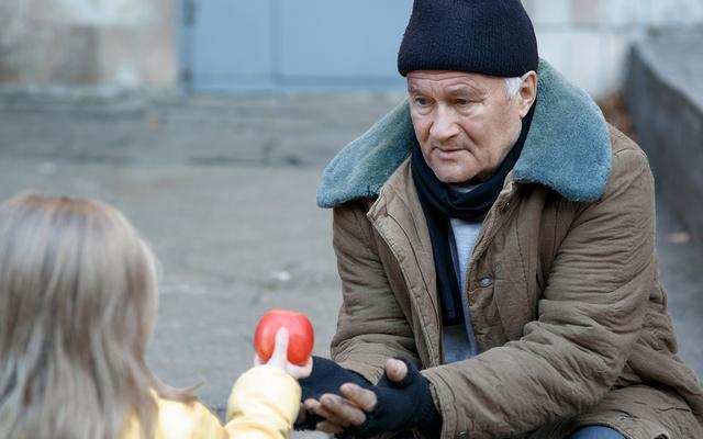 Mädchen reicht Obdachlosem einen Apfel