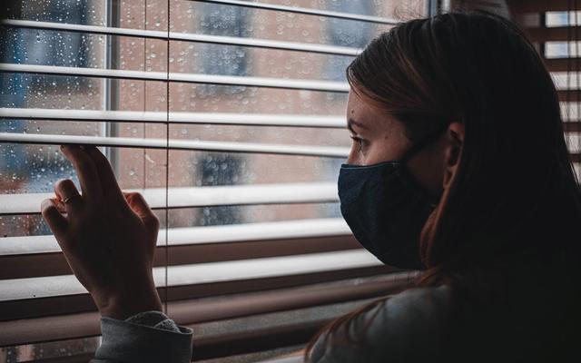 Frau mit Gesichtsmakse schaut aus dem Fenster
