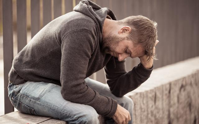 Junger Mann sitzt allein und traurig draussen.