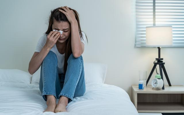 Junge Frau sitzt weinend im Bett