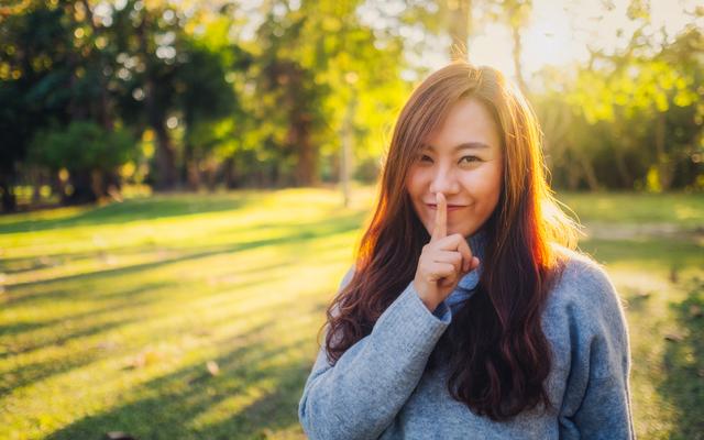 Asiatische Frau hebt den Zeigefinger an die Lippen