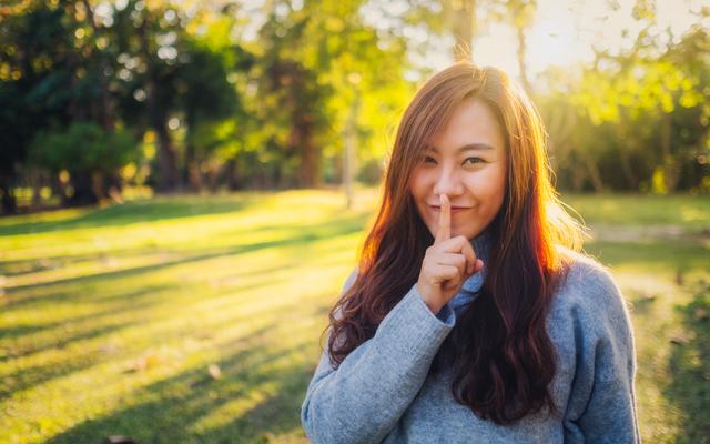 Asiatische Frau hebt den Zeigefinger an die Lippen