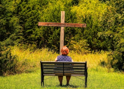 Frau sitzt auf einer Bank zum Holzkreuz