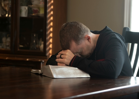 Ein Mann betet am Tisch mit seiner Bibel