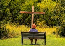 Frau sitzt auf einer Bank zum Holzkreuz
